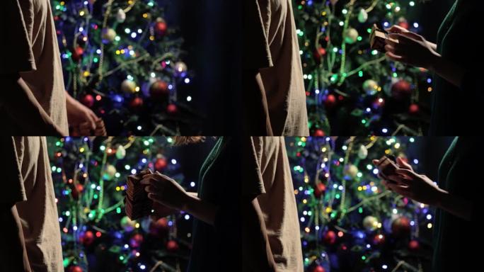 手中的圣诞礼物。穿着浅棕色t恤的男朋友给女孩穿绿色针织夹克，用老虎纸包裹，用黑色丝带绑在模糊新年树的