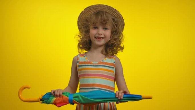 戴着草帽的可爱的卷发金发女孩拿着彩虹伞跳舞