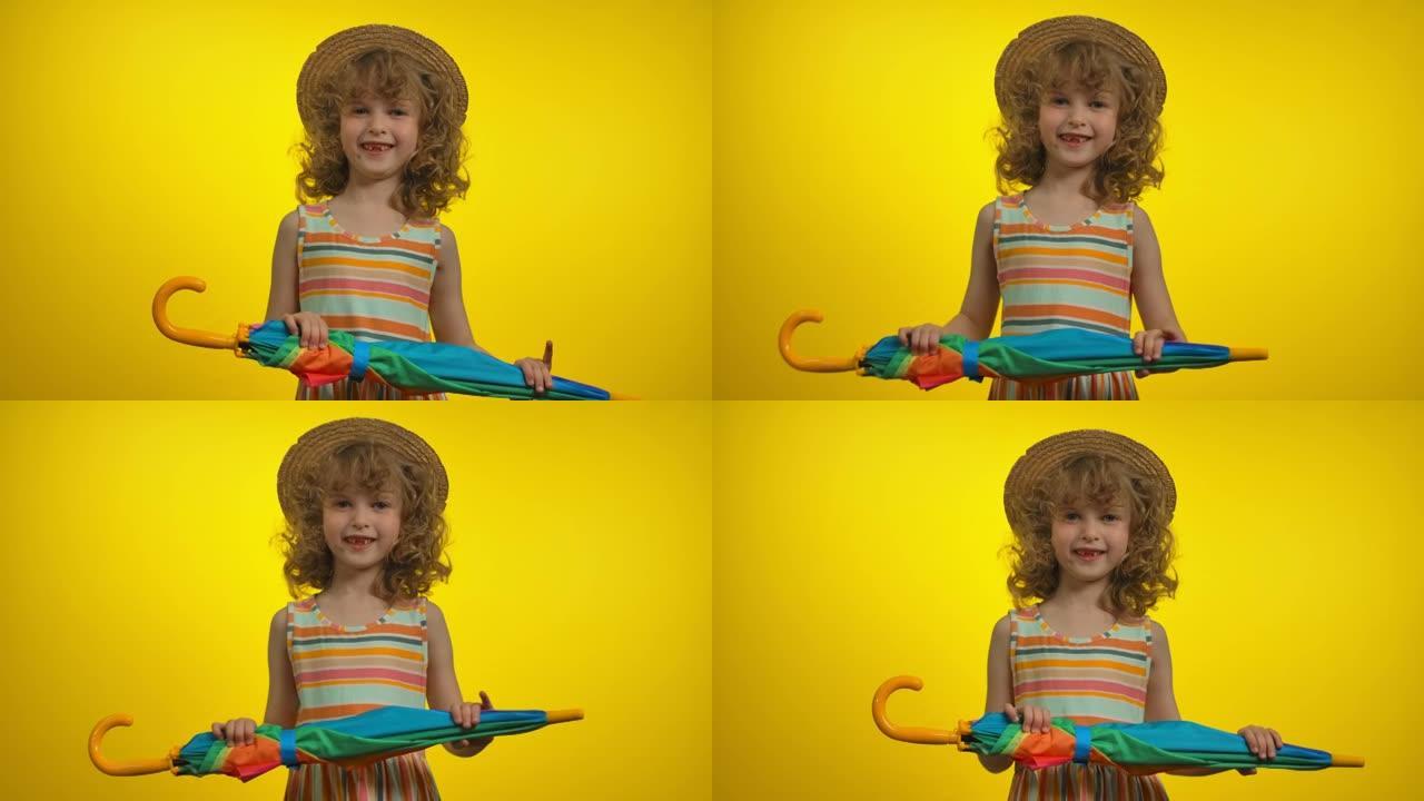 戴着草帽的可爱的卷发金发女孩拿着彩虹伞跳舞