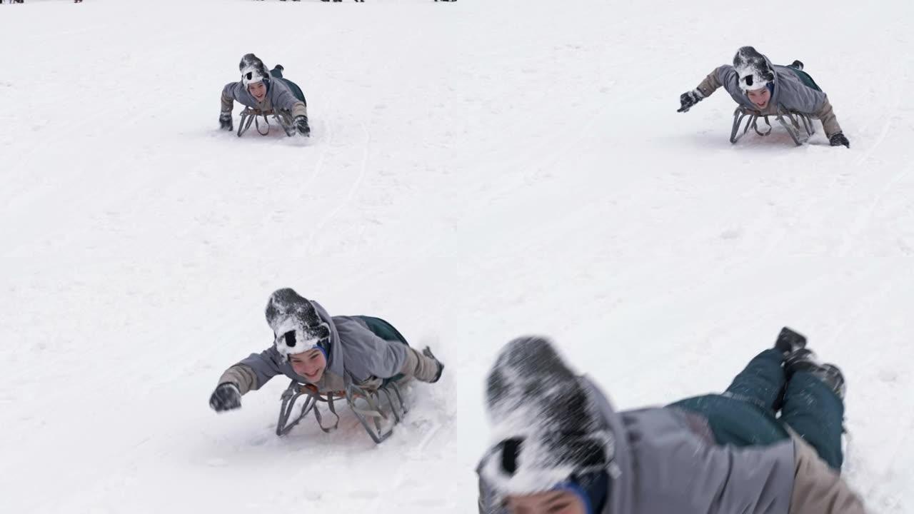 穿着滑雪服的开朗男孩在雪橇上滑下山坡，用手帮助自己。孩子快乐