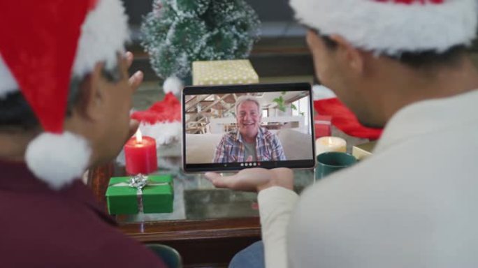 混血儿的父亲与儿子挥舞着，并使用平板电脑与屏幕上的男人进行圣诞节视频通话