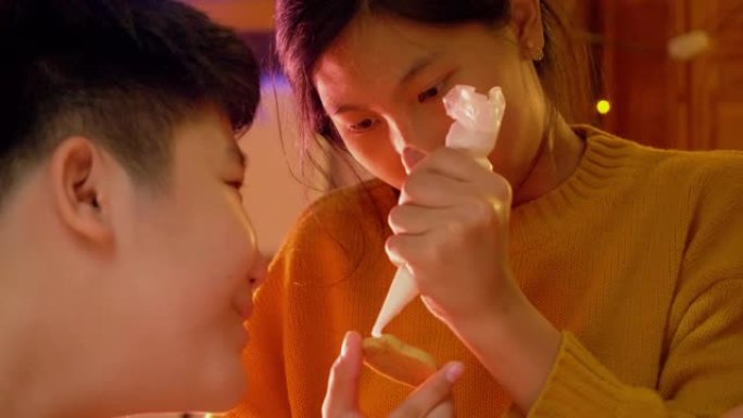 亚洲男孩看着他的妹妹在晚上在家一起装饰糖衣饼干，万圣节的生活方式概念。