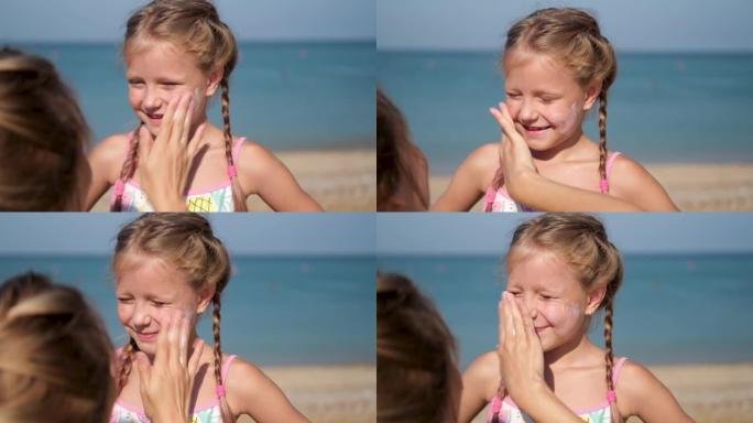 母亲在海滩上给女儿的脸上涂了防护霜。女人用手在婴儿脸上拿着防晒霜。海边有一个太阳挡的可爱的小女孩。
