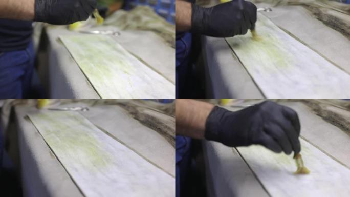 在工艺品修理厂使用刷子在工作台上的皮片上涂胶