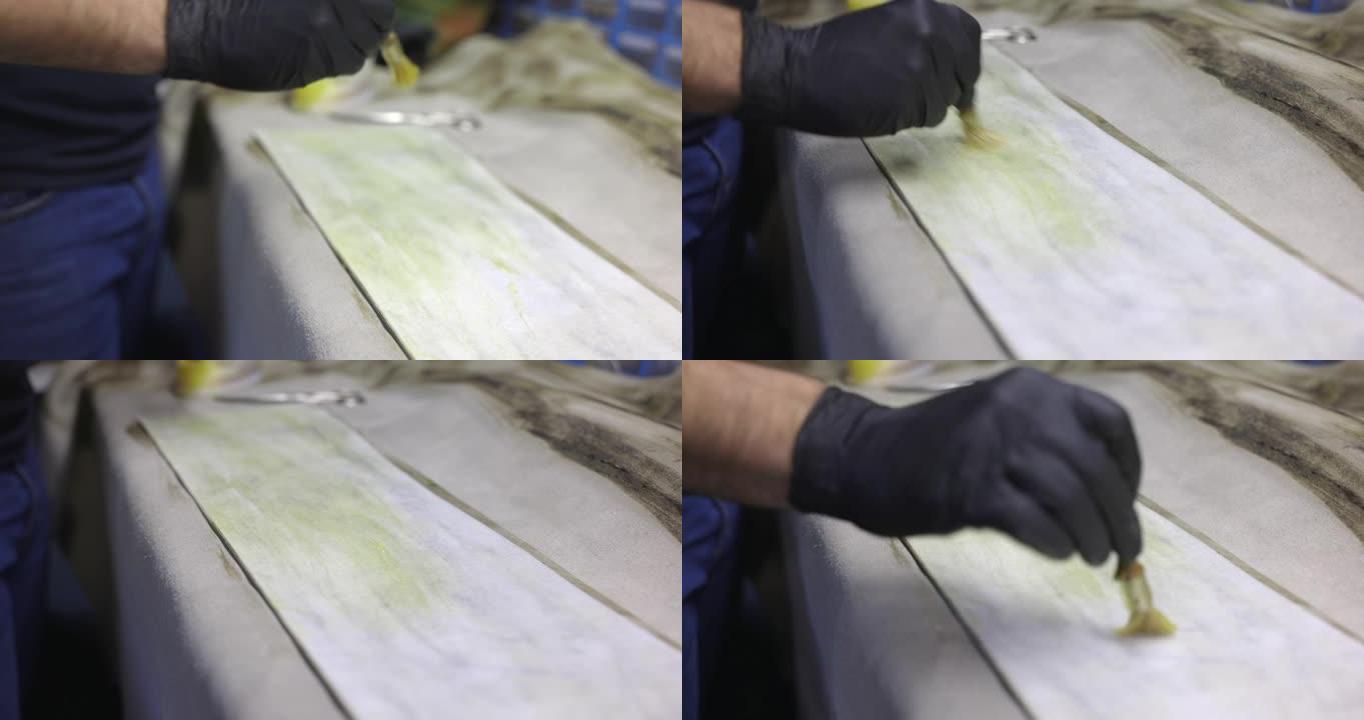 在工艺品修理厂使用刷子在工作台上的皮片上涂胶