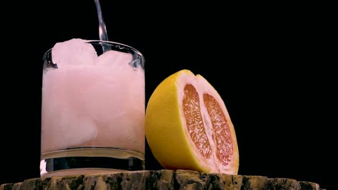 将葡萄柚汁倒在黑色背景的木制桌子上。将冰镇鸡尾酒倒入带有葡萄柚片的玻璃杯中。天然果汁。夏季冰镇饮料