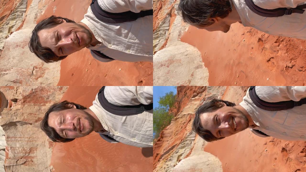 垂直视频。慢动作镜头。一名男子游客正在参观越南南部美内村沙漠边界的红色峡谷或仙女溪。在电话上开枪。
