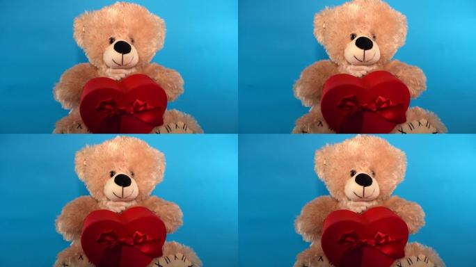 可爱的泰迪熊的特写镜头，红色礼品盒呈心形。蓝色背景的毛绒玩具。假期、礼物和好心情的概念