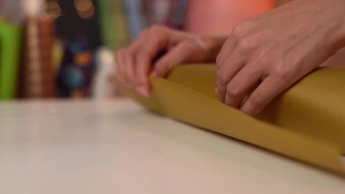年轻女子的特写手小心地将双面胶贴在金色包装纸上，用圣诞礼物包装节日纸板箱。