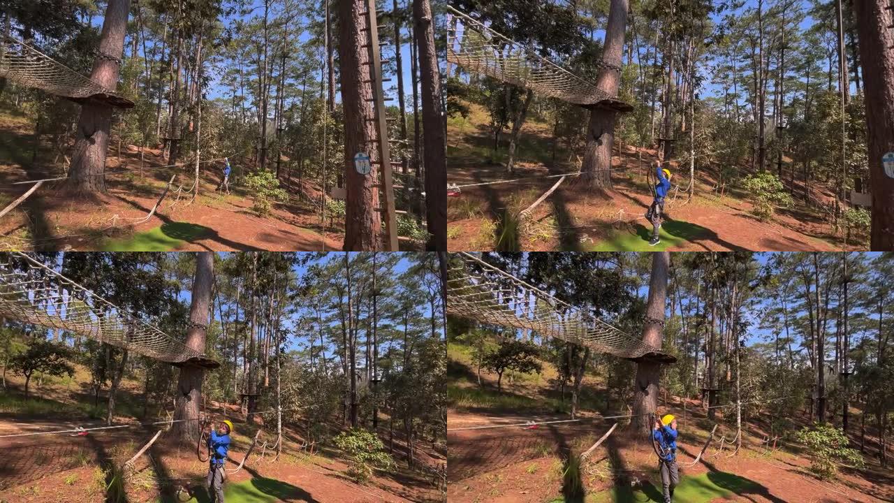 一个戴着黄色头盔的男孩的慢动作拍摄，该男孩在爬绳冒险公园里玩得很开心。在电话上拍摄
