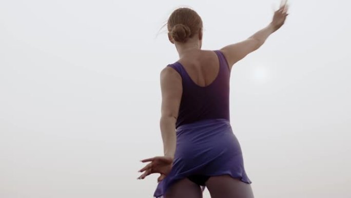 女芭蕾舞女演员训练舞蹈户外背景天空，后视图。舞者正在外面练习她的舞蹈。女人穿着运动服跳舞