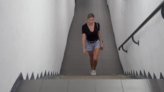 一名年轻女子独自沿着地下通道行走，爬上楼梯。去见摄像机。