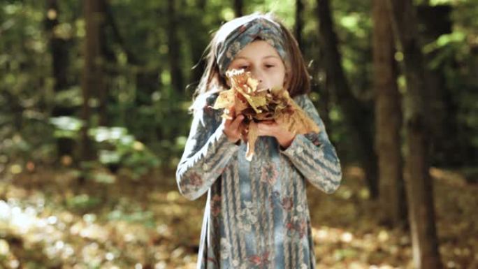 小女孩在公园里玩秋天的落叶。孩子笑着吐橙色枫叶。一个有秋叶的孩子的肖像。可爱的孩子在秋天的草地上抱着