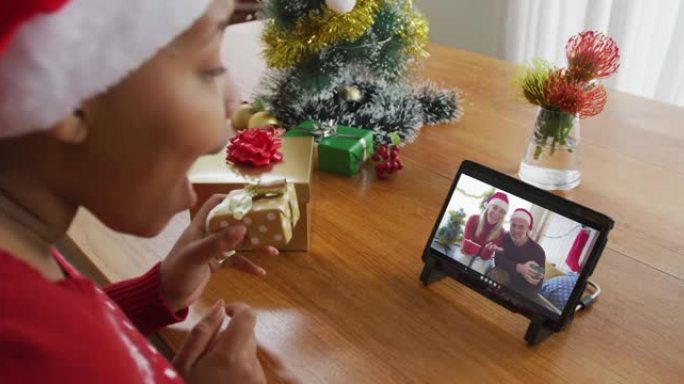 戴着圣诞老人帽子的非洲裔美国妇女使用平板电脑进行圣诞节视频通话，屏幕上有家人