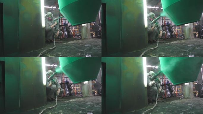 工厂室内的工业喷漆工艺。油漆工在特殊的展位上喷涂绿色油漆。安全磨损技术人员在生产中工作。专业车间的油