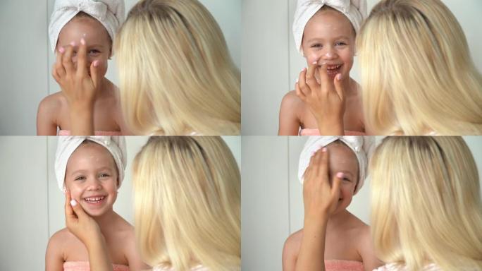 母亲在洗澡后将面霜涂在女儿的脸上。婴儿护肤
