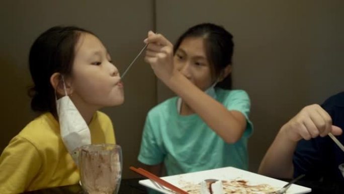 亚洲女孩在餐厅为姐姐喂巧克力冰淇淋圣代，生活方式概念。