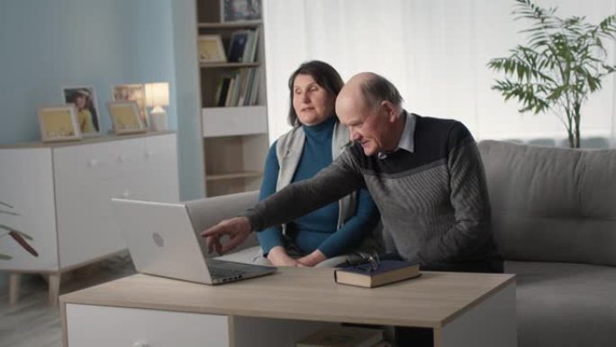 恩爱的老年夫妇一起玩得开心，坐在客厅的沙发上浏览笔记本电脑上的网上购物