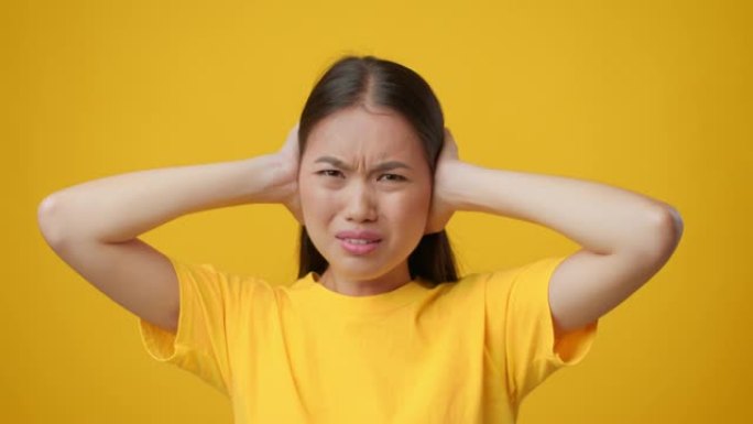 亚洲女人捂着耳朵用手摇头，黄色背景