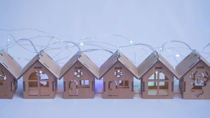 木制玩具屋排成一排。房子里的花环和灯亮着。电的出现的概念。圣诞节假期用照明装饰房屋的概念