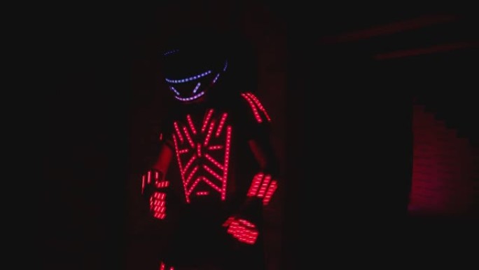 男人穿着照明服装，五颜六色的发光二极管灯在黑暗的室内或俱乐部里跳舞和移动。舞者家伙穿着带有霓虹灯的衣