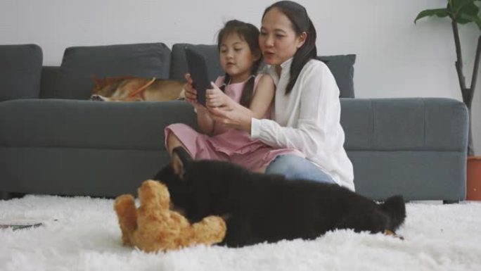 亚洲母女使用数字平板电脑与狗一起学习。家庭在室内休息。