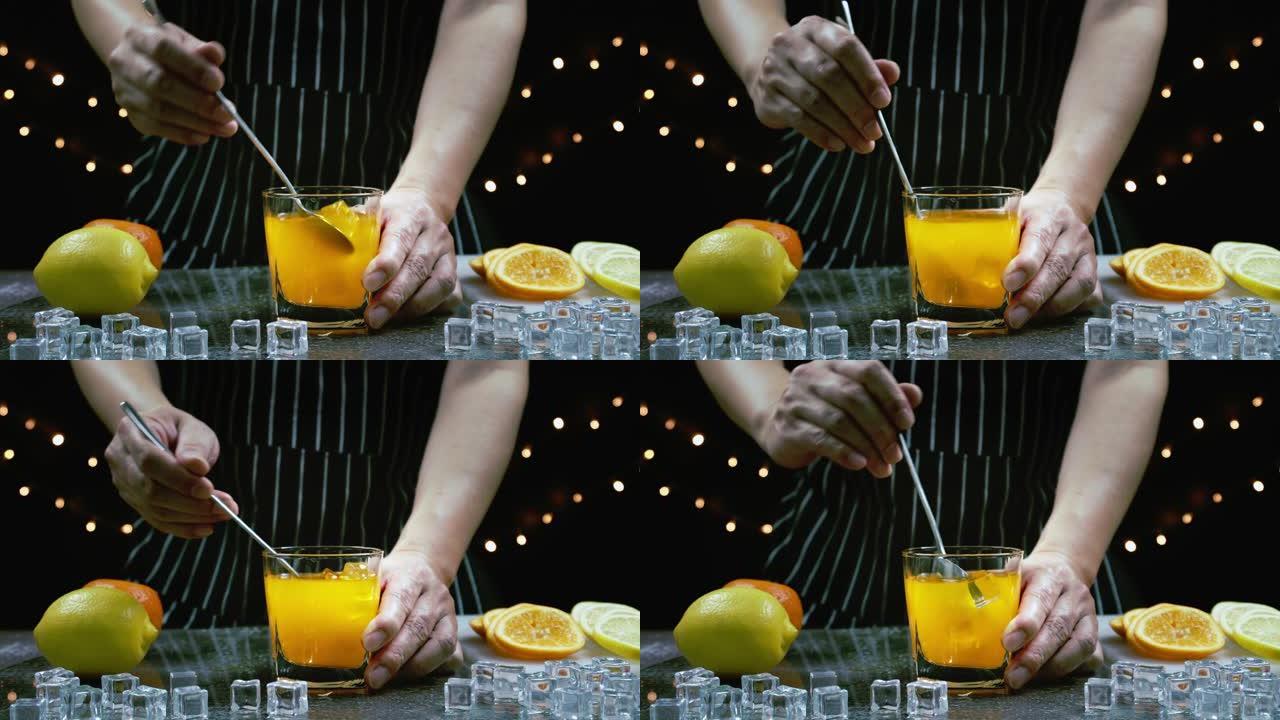 男子抓住玻璃杯，在桌子上的新鲜柠檬和橙子附近搅拌冰和橙子