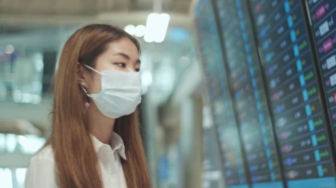 戴着医用口罩的亚洲妇女在机场检查出发板