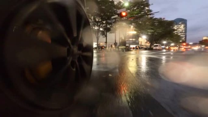 在雨夜开车穿过城市。汽车车轮的特写。在人们正在穿越的十字路口右转