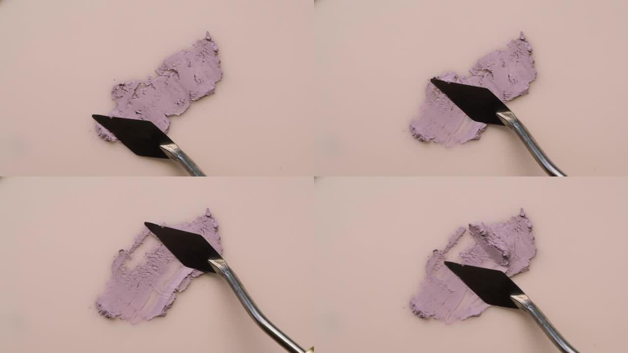 在米色背景上涂抹紫色奶油，样品粉底纹理特写。化妆品和美容产品概念，化妆品，眼影调色板，古铜色或遮瑕