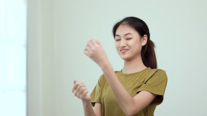 迷人的亚洲年轻健身女子伸展手臂在家锻炼前热身。美丽微笑的女性穿着运动服在客厅锻炼瑜伽。