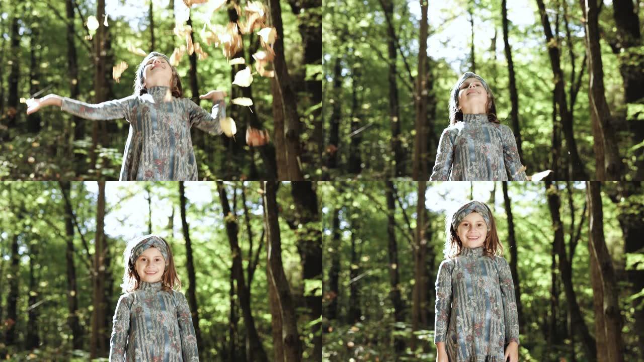 女孩在公园里把五颜六色的秋叶抛向空中。有趣，开朗可爱的小女孩吐了一个黄色的秋天落叶慢动作