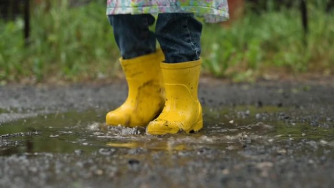 一个穿着黄色胶靴的孩子在雨中在水坑里奔跑和玩耍