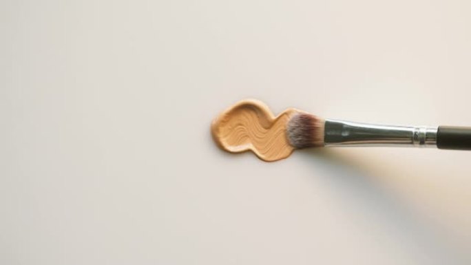 在白色背景上涂抹底色。棕色奶油纹理特写，使用笔刷。化妆品和美容产品概念，化妆品，眼影调色板，古铜色或