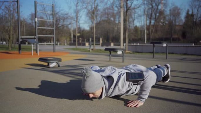 运动的年轻人在户外街头健身场所做各种各样的肩膀轻拍俯卧撑，臂章上有手机