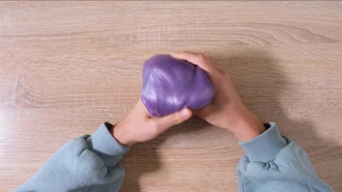 玩粘液，拉伸粘稠物质以获得乐趣和缓解压力。特写和俯视图的女性手拿着紫色闪亮的粘液并挤压它。4k视频。