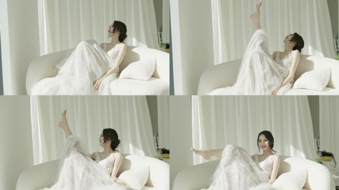 穿着白色婚纱的美丽亚洲新娘，坐在沙发上，开心的表情，慢动作拍摄