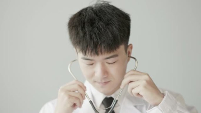 年轻的亚洲男医生，身穿白大褂，听诊器，对着镜头微笑，特写脸部，慢动作