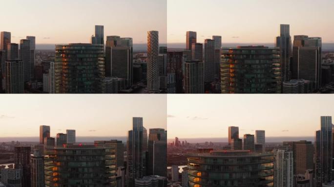巴尔的摩塔顶的滑动和平移镜头。圆柱形公寓楼，四周有露台。金丝雀码头自治市镇的摩天大楼和日落时间的城市