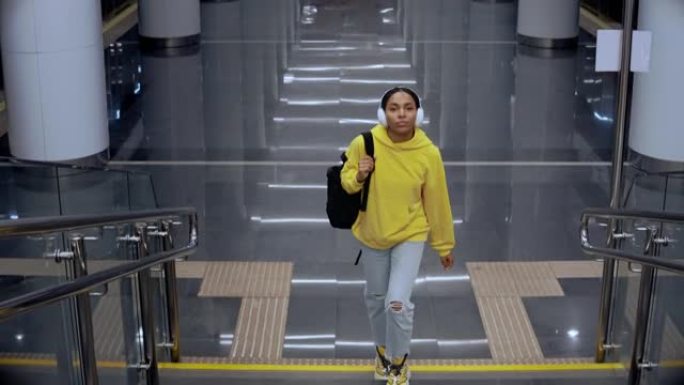 年轻的女孩戴着耳机在现代火车站上楼梯