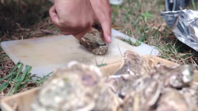 没有手套的男人用烹饪刀在塑料烹饪板上打开牡蛎壳，男人试图从地中海鱼市场打开新鲜的生牡蛎。豪华海洋熟食