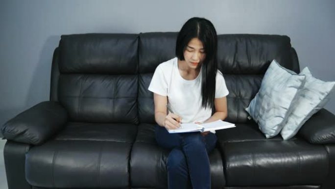 亚洲女性在沙发上写作和看书