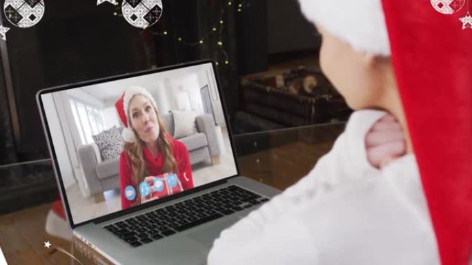 在与家人的笔记本电脑视频通话中，雪花落在圣诞老人帽子上的微笑女人身上的动画