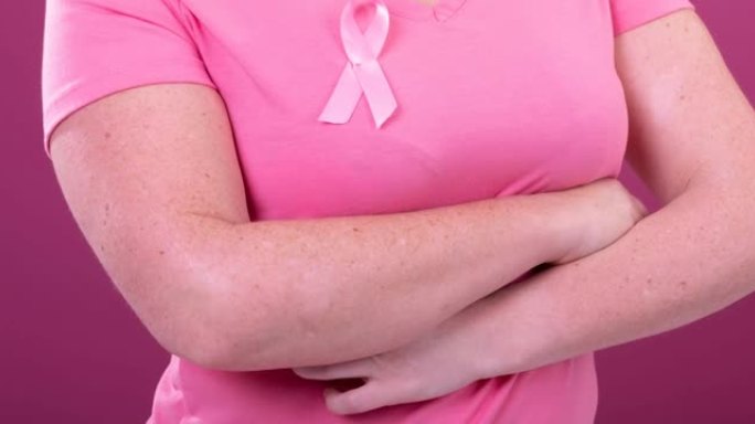 视频上腹部的白人妇女穿着粉红色的癌症意识丝带，粉红色的背景