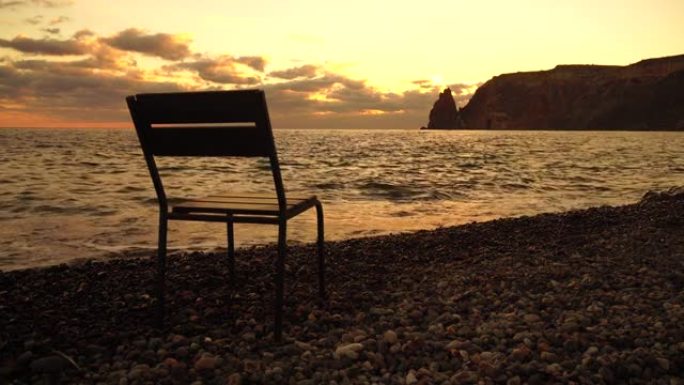 日落时海滩上戏剧性的海景，前景是空椅子，温暖的日落照亮了岩石火山悬崖。没人。平静沉默与自然统一的概念
