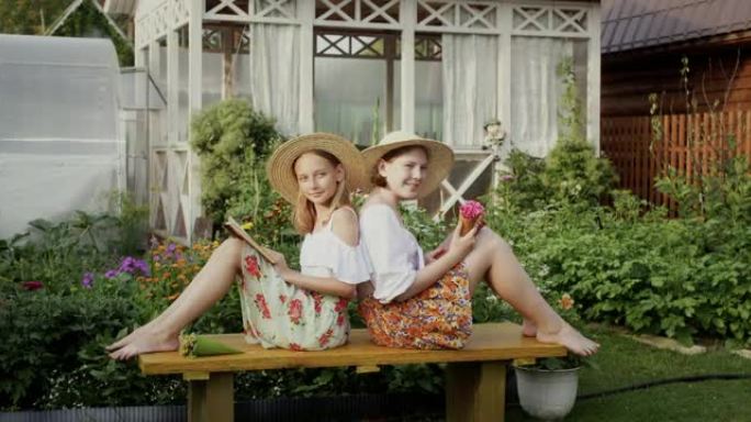 开朗的农村少女在农村的木凳上一起读书。暑假时，浪漫的女孩青少年在乡村长凳上看书和鲜花。