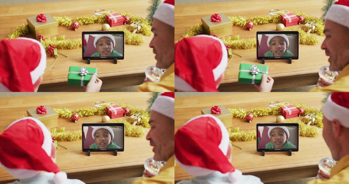 白人父亲和儿子戴着圣诞老人的帽子，使用平板电脑与屏幕上的男孩进行圣诞节视频通话