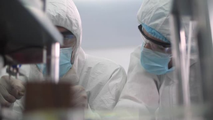 两家研究医用口罩工厂洁净室，工程师和科学家穿着工作服与数字平板电脑交谈