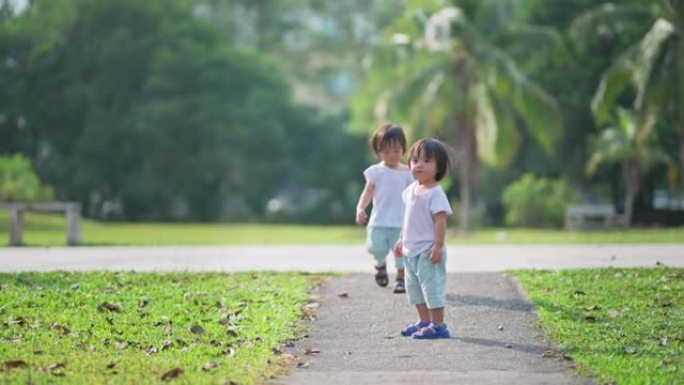 周末早上，亚洲中国双胞胎男婴在公园草坪上走向相机