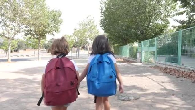 一个黑头发的女孩和另一个背着金色头发的女孩，背着背包，走在上学的路上。教育和返校理念。
